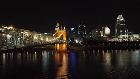 Flying-parallel-to-the-lit-Roebling-Bridge-with-the-Cincinnati-skyline-in-the-background---Aerial-view