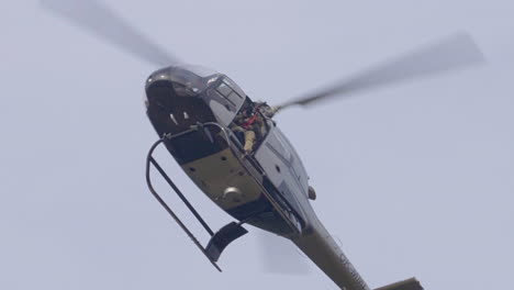 Military-Helicopter-With-Soldier-Holding-Sniper-Rifle-Flying-in-the-Sky,-Low-Angle