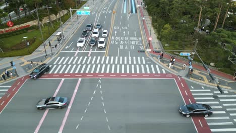 Pedestrians-and-cars-waiting-and-crossing-an-intersection-near-Lotte-World-Tower,-Seoul,-South-Korea