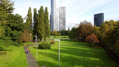 Manchester-city-parkland-aerial-view-flying-above-trees-to-view-modern-high-rise-skyline