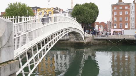 La-Gente-Cruza-En-El-Puente-De-Arco-De-Medio-Centavo-Sobre-El-Río-Liffey-En-La-Ciudad-De-Dublín,-Irlanda