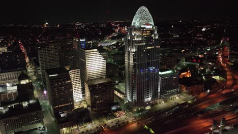 Aerial-view-in-front-of-the-Great-American-Tower-and-traffic-on-Interstate-71-US-50,-night-in-Cincinnati,-USA---reverse,-tilt,-drone-shot