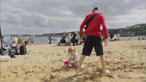 Bruder-Und-Schwester-Spielen-Im-Sand-Am-Strand-Kleines-Mädchen-Füllt-Einen-Eimer-Mit-Sand-Scarborough-Uk