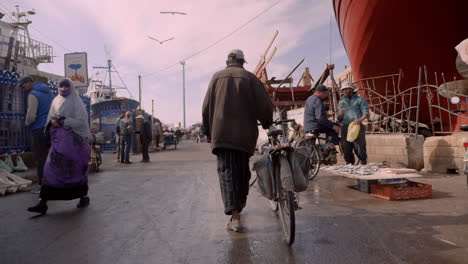 Moroccan-man-walks-next-to-his-bicycle-in-port-city-of-Essaouira,-Morocco