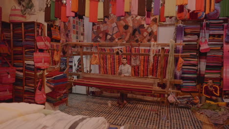 Young-man-weaves-textile-in-a-family-artisanal-shop-in-Fes,-Morocco