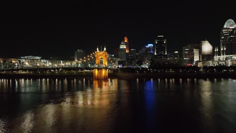 Luftaufnahme-Tief-über-Dem-Fluss-Mit-Der-Beleuchteten-Skyline-Von-Cincinnati-Im-Hintergrund