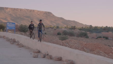 Dynamic,-documentary-shot-of-poor-moroccan-kids-playing-with-a-used-tire-on-a-small-wall-on-the-side-of-the-road