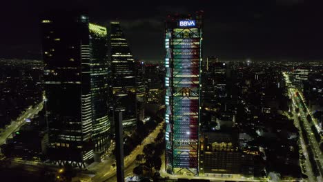 Vista-Aérea-Alrededor-De-La-Torre-Bbva-Iluminada-Con-Los-Colores-De-La-Bandera-Mexicana,-Día-De-La-Independencia-En-La-Ciudad-De-México---Dando-Vueltas,-Tiro-Con-Drones