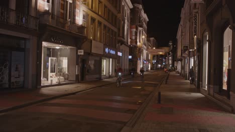 Static-view-of-cyclists-driving-through-shopping-district-in-Ghent,-Belgium-at-night