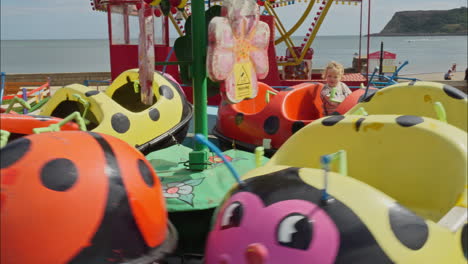 Niño-En-Un-Paseo-En-Carrusel-De-Mariquitas-En-Un-Parque-De-Diversiones-Junto-Al-Mar-En-Scarborough,-Reino-Unido