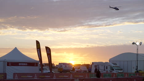 Ein-Feuerorangefarbener-Sonnenaufgang-Und-Ein-Einsamer-Helikopter,-Der-über-Dem-Dakar-Rallye-Offiziellen-Fliegt