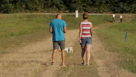 A-man-and-a-woman-with-a-small-dog-walk-along-Lake-Lapovac,-Croatia,-Europe