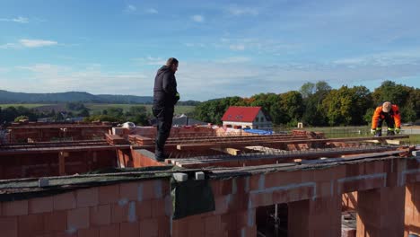 Building-new-roof,-aerial-drone-side-closeup-view-of-workers,-sunny-day