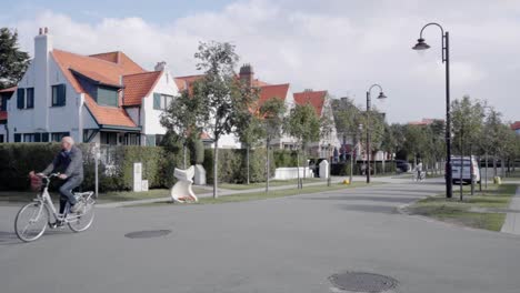 Hombre-Mayor-En-Bicicleta-A-Lo-Largo-De-Las-Casas-Residenciales-En-El-Famoso-Barrio-De-Concesión-En-De-Haan,-Bélgica