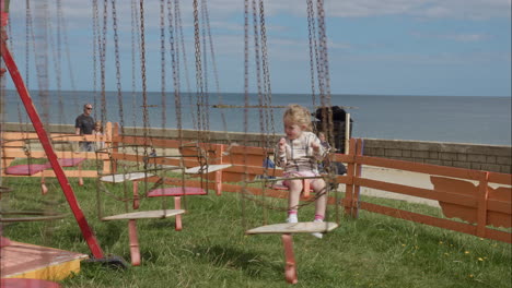 Child-girl-rides-chain-swing-carousel-merry-go-round-at-seaside-amusement-park-bright-sunny-day-during-summertime-in-August-2022