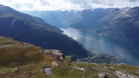 Impresionantes-Vistas-Aéreas-Desde-La-Ruta-De-Senderismo-De-Dronningstien-Queens-Con-El-Pueblo-De-Lofthus-Muy-Por-Debajo-Del-Acantilado-Escarpado---Amigos-Descansando-En-El-Borde-Del-Acantilado---Vista-Reveladora-Del-Fiordo-Con-Efecto-De-Paralaje