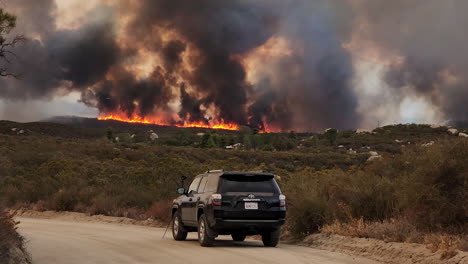 Vehículo-Todoterreno-Estacionado-En-Camino-De-Tierra,-Cámara-En-Trípode-Filmando-Las-Dramáticas-Columnas-Oscuras-De-Humo-De-Incendios-Forestales,-Cámara-Lenta