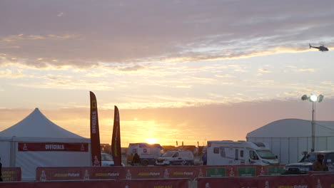 Vista-Del-Vivac-Del-Rally-Dakar-Al-Atardecer-Con-Helicóptero-Cruzando-El-Cielo