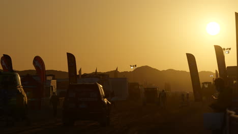 Feuriger-Orangefarbener-Sonnenaufgang-über-Dem-Hauptlager-Von-Paris-Dakar-Mit-Einfahrenden-Fahrzeugen