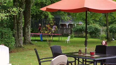 Shot-of-two-children-running-around-and-others-jumping-on-trampoline-in-the-garden-at-daytime