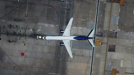 Vehículo-Remolcador-De-Empuje-Que-Ayuda-A-Un-Avión-En-La-Salida---De-Arriba-Hacia-Abajo,-Vista-Aérea