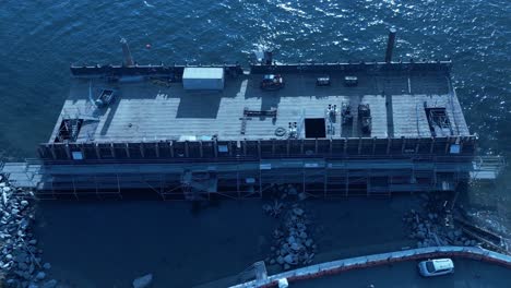 Vancouver-barge-removal-and-deconstruction-Drone-aerial-fly-into-close-up-of-vessel-turfed-and-stuck-next-to-the-seawall-people-walking-by-the-path-with-fencing-barriers-separating-crew-minivan-parked