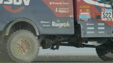 A-distant-helicopter-flying-away-above-the-desert-and-dakar-rally-traffic-passing-through-foreground-road