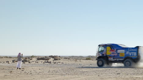 Un-Hombre-árabe-Solitario-Filmando-Un-Camión-De-Rally-Dakar-Corriendo-Con-Nubes-De-Polvo