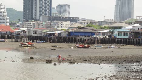 Traditional-Thai-style-residential-houses-along-the-coast-of-Si-Rascha,-the-outgoing-tide-leaves-the-local-fisherman's-boats-beach-on-the-sand,-Thailand