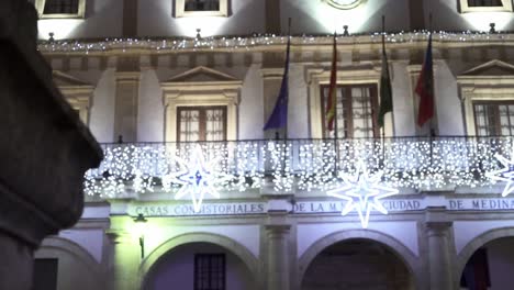 Toma-Panorámica-En-Cámara-Lenta-De-La-Columna-De-Una-Pared-Durante-La-Toma-De-Seguimiento-Del-Ayuntamiento-Casa-Consistorial-De-Medina-Sidonia-En-Cádiz-En-España-Con-Balcón-Decorado-Con-Luces-Y-Elementos-Navideños