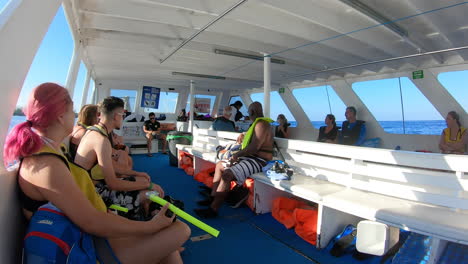 Professional-diver-giving-life-jacket-demonstration,-instructions-to-tourists-in-boat-before-going-to-dive-in-ocean-|-Life-jacket-training-and-instructions-to-and-tourists