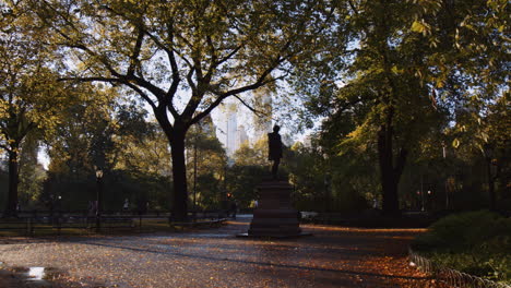 Urban-Park,-Statue-Sculpture-Monument-Surrounded-By-Trees-in-Central-Park-New-York-City-in-Sunny-Morning,-People-Walking-Running-in-Park