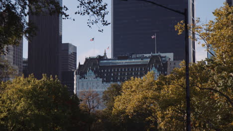 Blick-Auf-Das-Majestätische-Plaza-Hotelgebäude-Vom-Central-Park,-New-York-City,-Manhattan,-USA,-Umgeben-Von-Modernen-Gebäudetürmen,-Städtische-Parkbäume,-Vegetation-Im-Vordergrund