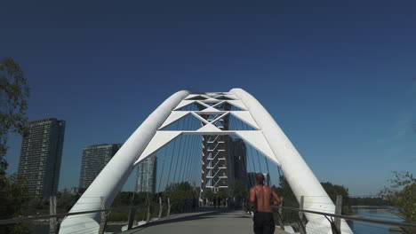 Amplia-Toma-Exterior-En-Movimiento-Siguiendo-A-Un-Corredor-Que-Se-Acerca-Al-Puente-De-Arco-De-Humber-Bay.