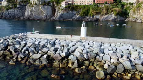 Foto-De-Dronie-De-Una-Pareja-Sentada-Junto-Al-Faro-En-Camogli,-Famosa-Atracción,-Genova