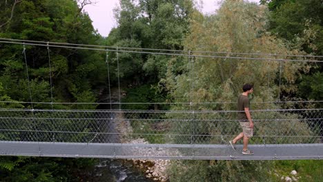 Joven-Cruzando-El-Puente-Colgante-Tibetano-En-La-Naturaleza-Verde-Sobre-El-Río,-Turín,-Italia