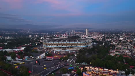 Aerial-view-towards-the-Estadio-Azteca-stadium,-sunset-in-Mexico-City---rising,-drone-shot