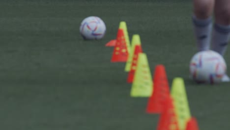 Female-soccer-practice-with-ball-dribbling-around-cones-in-stadium