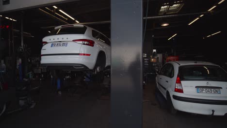 the-interior-of-a-car-garage-seen-from-the-outside-with-two-white-cars,-one-of-which-is-high-up-for-examination