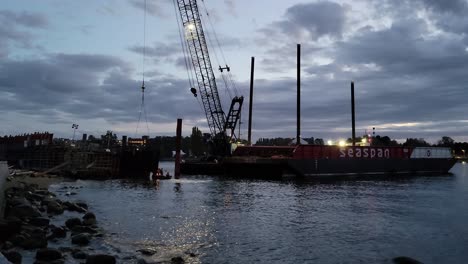 Ein-Team-Von-Leuten,-Die-Bei-Sonnenuntergang-Arbeiten-Und-Einen-Massiven-Lastkahn-Demontieren,-Der-Vom-Sturm-An-Der-Ufermauer-Der-Englischen-Bay-In-Vancouver,-Kanada,-Angeschwemmt-Wurde