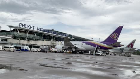 Ver-Cámara-Lenta-Dentro-De-La-Bahía-De-Estacionamiento-Del-Aeropuerto-Con-Un-Avión-Boeing-Mientras-La-Carga-Del-Servicio-Terrestre-Opera-En-Un-Día-De-Lluvia