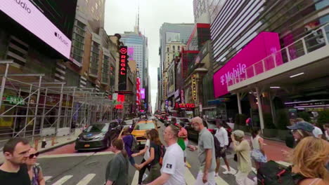 Crossing-a-busy-street-in-Manhattan,-New-York-while-a-yellow-cab-waits-at-red