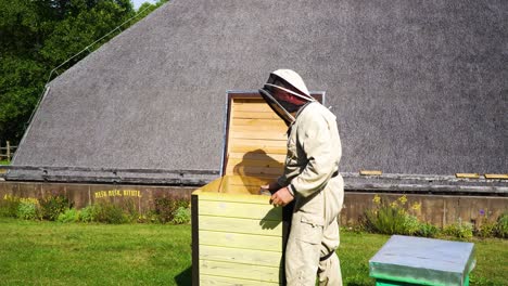 Beekeeper-in-a-full-uniform-working-and-checking-on-the-beehive