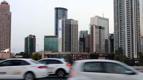 Slow-moving-car-lines-in-traffic-jam-in-large-modern-city-with-skyscrapers,-Tel-Aviv-Israel