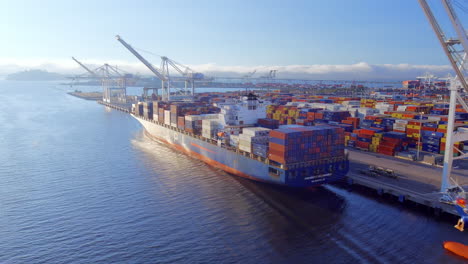 Cargo-container-ships-in-the-Port-of-Oakland,-California-being-loaded-or-unloaded-using-cranes-on-the-dock---aerial-pull-back-flyover