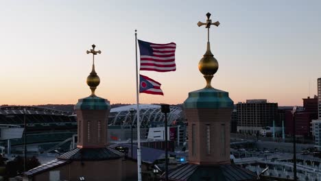 Vista-Aérea-Alrededor-De-La-Bandera-De-Ohio-Y-Estados-Unidos-En-El-Puente-Roebling-Con-El-Fondo-Del-Horizonte-De-Cincinnati-Al-Atardecer---Dando-Vueltas,-Tiro-De-Drones-En-Cámara-Lenta