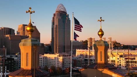 Flags-waving-in-front-of-a-city-background,-sunny-evening-in-USA---Aerial-view