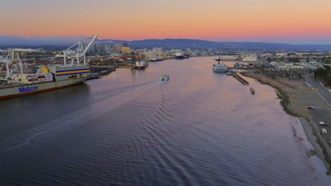 Vista-Aérea-Siguiendo-El-Ferry-De-San-Francisco-Alameda-Navegando-Por-El-Puerto-Marítimo-De-Oakland-Al-Atardecer