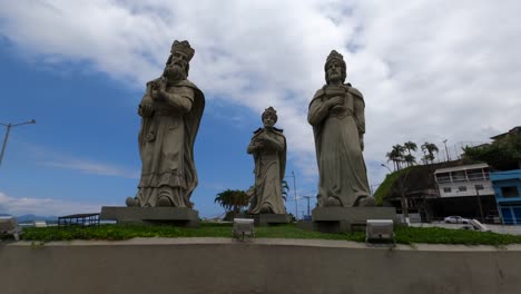 Angra-dos-Reis,-Rio-de-Janeiro,-Brazil---October-17,-2022-Time-Lapse-of-the-Statue-of-the-three-wise-men-in-Angra-dos-Reis-with-car-and-pedestrians-on-Avenida-Ayrton-Senna-in-Angra-dos-Reis