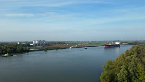 Antenne,-Die-über-Die-Baumgrenze-In-Richtung-Oude-Maas-Fliegt,-Mit-Blick-Auf-Schlepper,-Die-Sea-Prajna-Bulk-Ship-Entlang-In-Puttershoek-Unterstützen